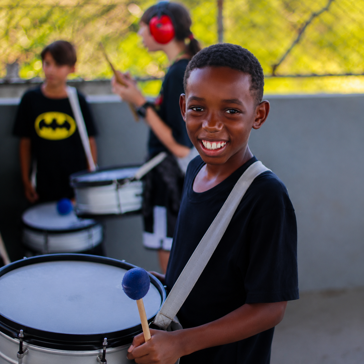 Aluno sorrindo com instrumento de percussão em atividade musical.